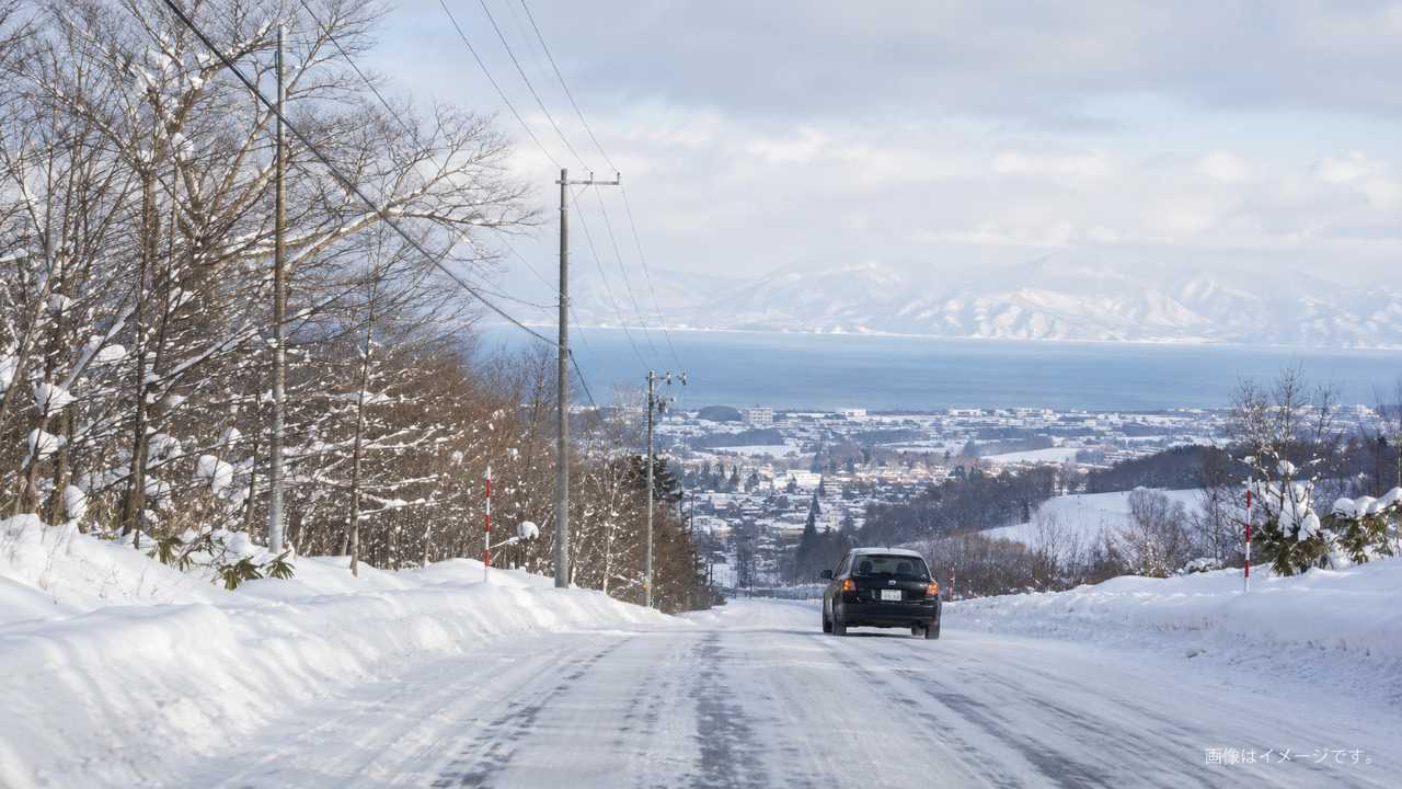 北海道の山あいへ向かう雪道、ニセコや小樽方面を連想させる坂道、慎重に走る車