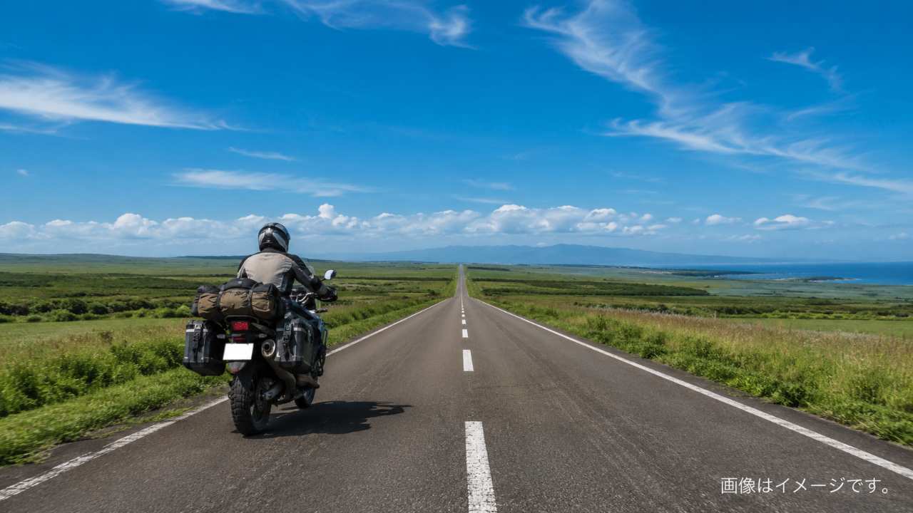 北海道の広大な直線道路を、荷物を積んだアドベンチャーバイクが走っている実写風